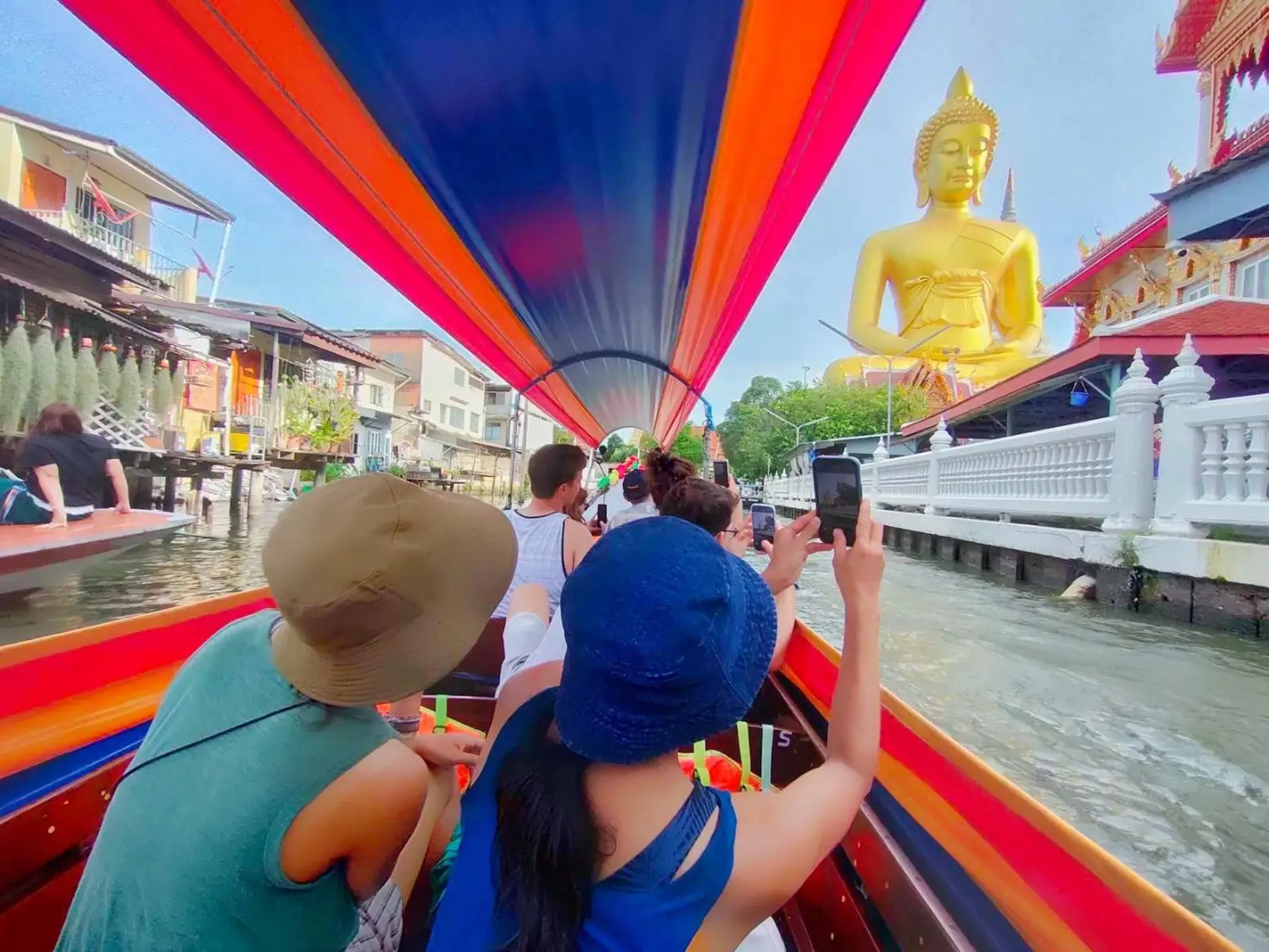 Traditional Thai longtail boat cruising through narrow Bangkok canal flanked by tropical trees and wooden stilt houses on a classic bangkok boat tour in Thonburi