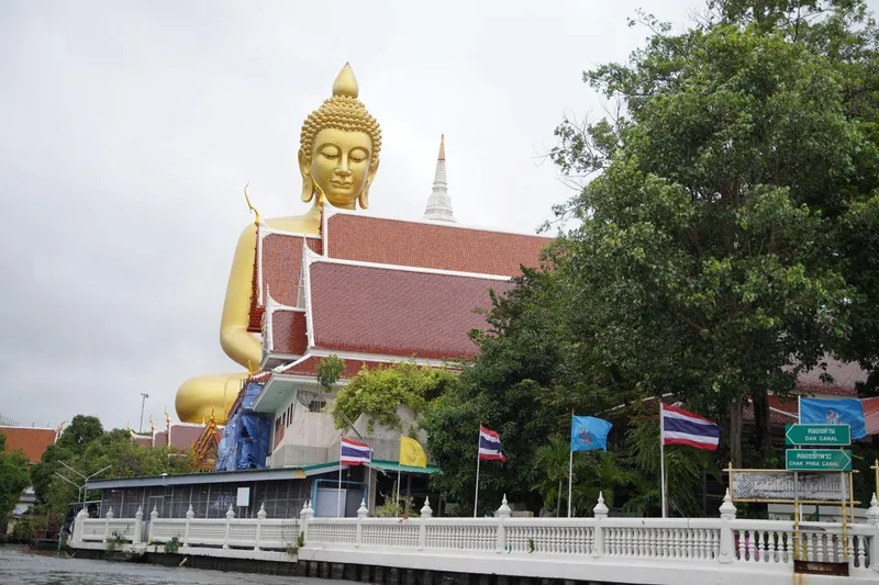 A traditional wooden teak boat on the Chao Phraya River with Wat Arun temple spires in the background on a bangkok canal tour